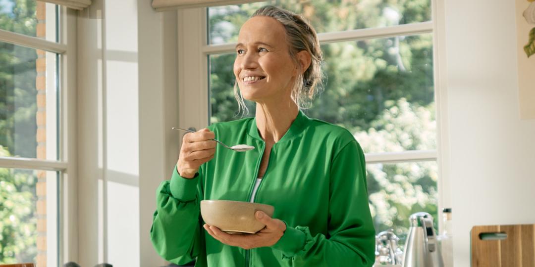 Vrouw eet schaaltje yoghurt in de keuken.