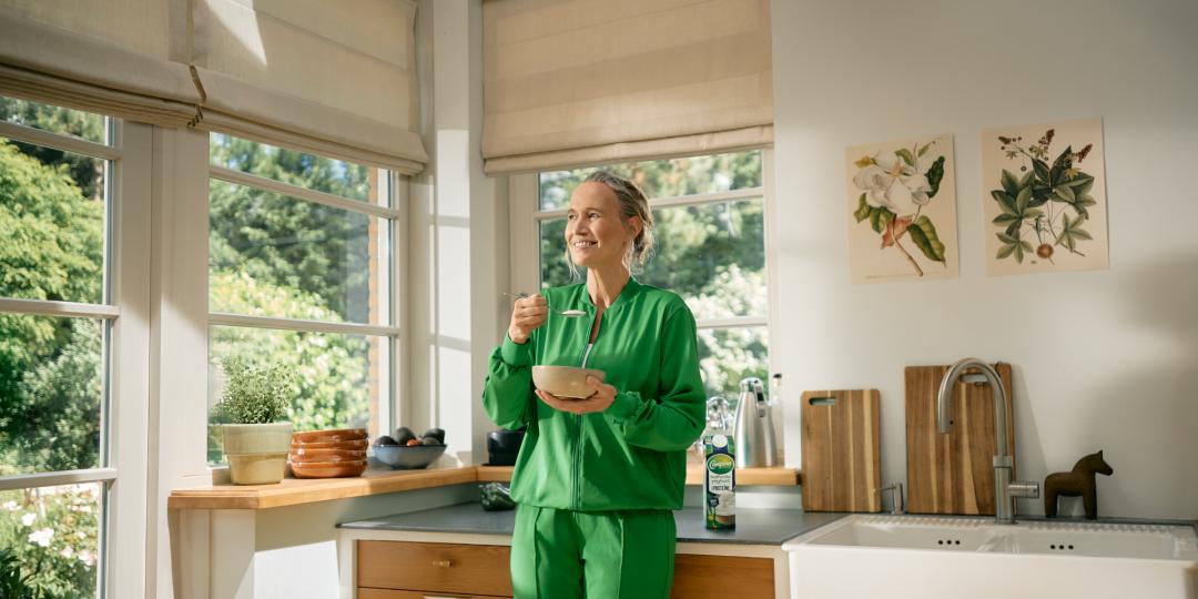 Vrouw eet schaaltje yoghurt in de keuken.