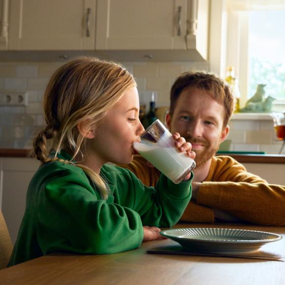 Meisje drinkt uit een glas terwijl vader toekijkt.